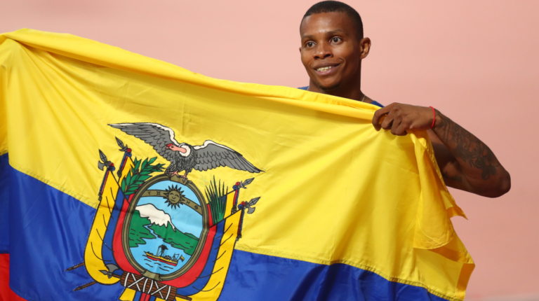 organismos Álex Quiñónez celebra su tercer lugar en el Mundial de atletismo en Doha, con la bandera de Ecuador.