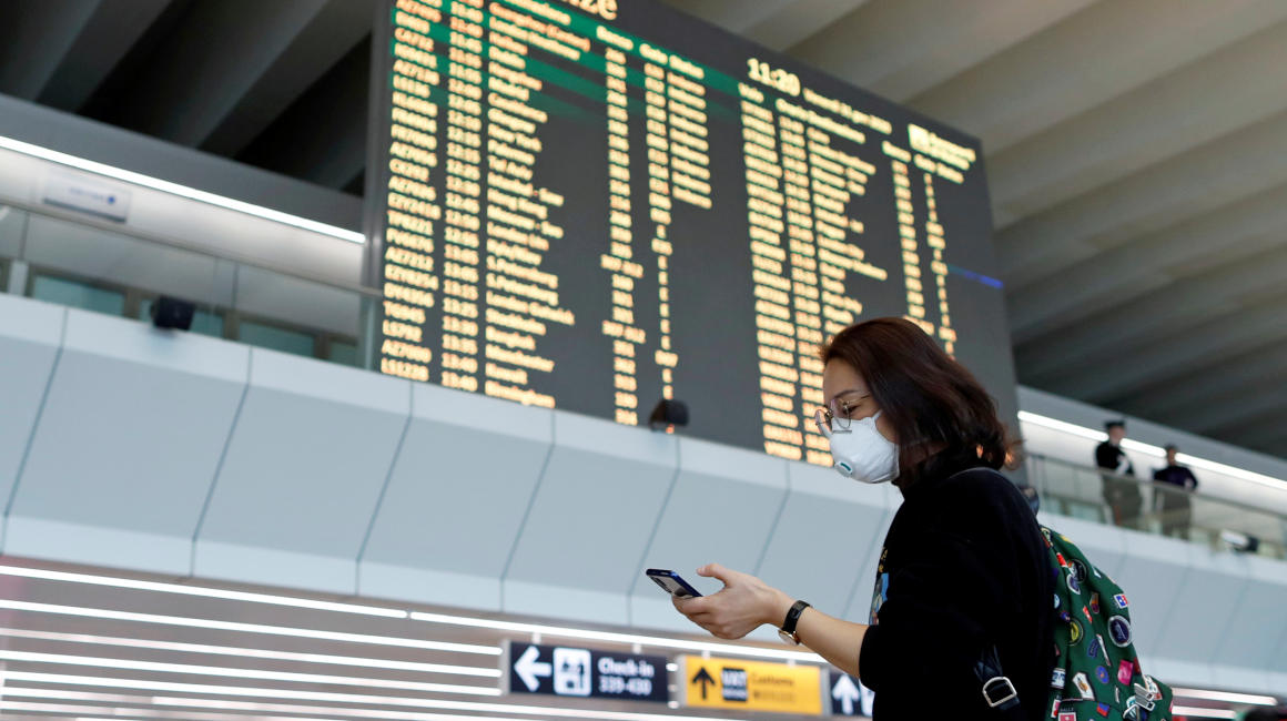 Una turista lleva una máscara de protección mientras utiliza su teléfono en el aeropuerto de Roma, en Italia, como medida de prevención ante el coronavirus de Wuhan.