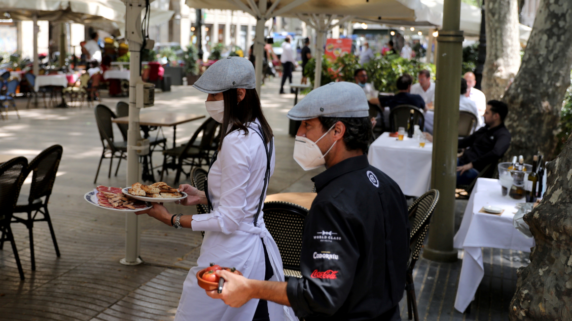 Meseros que usan mascarillas llevan comida para los clientes en un restaurante al aire libre en las Ramblas, en Barcelona, España, este lunes 25 de mayo.