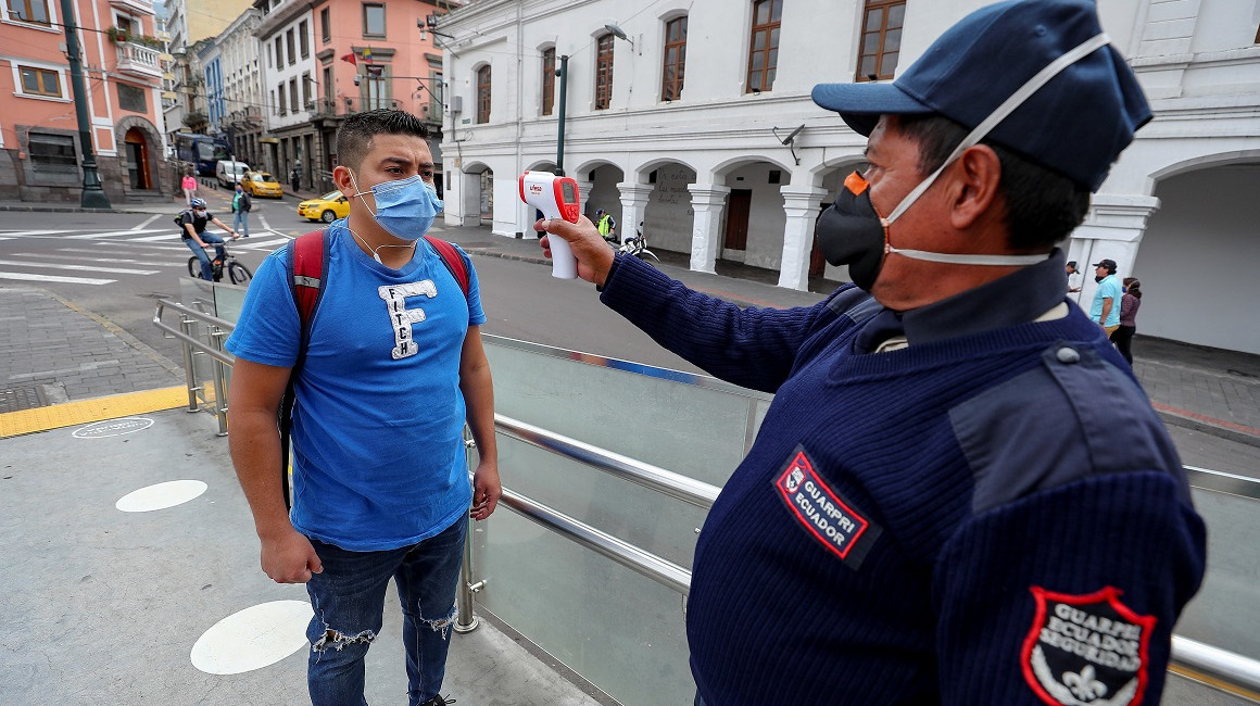 Un guardia de seguridad le toma la temperatura a un ciudadano en Quito antes de subirse a un bus de transporte público, el 10 de junio. 