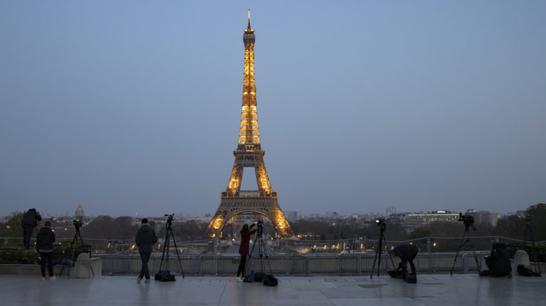Periodistas y fotógrafos mantienen una distancia entre ellos, mientras esperan que la palabra 'Merci' (Gracias) se proyecte en la Torre Eiffel para honrar a todo el personal que contribuye al esfuerzo de combatir el coronavirus, en París, Francia, el 27 de marzo de 2020.