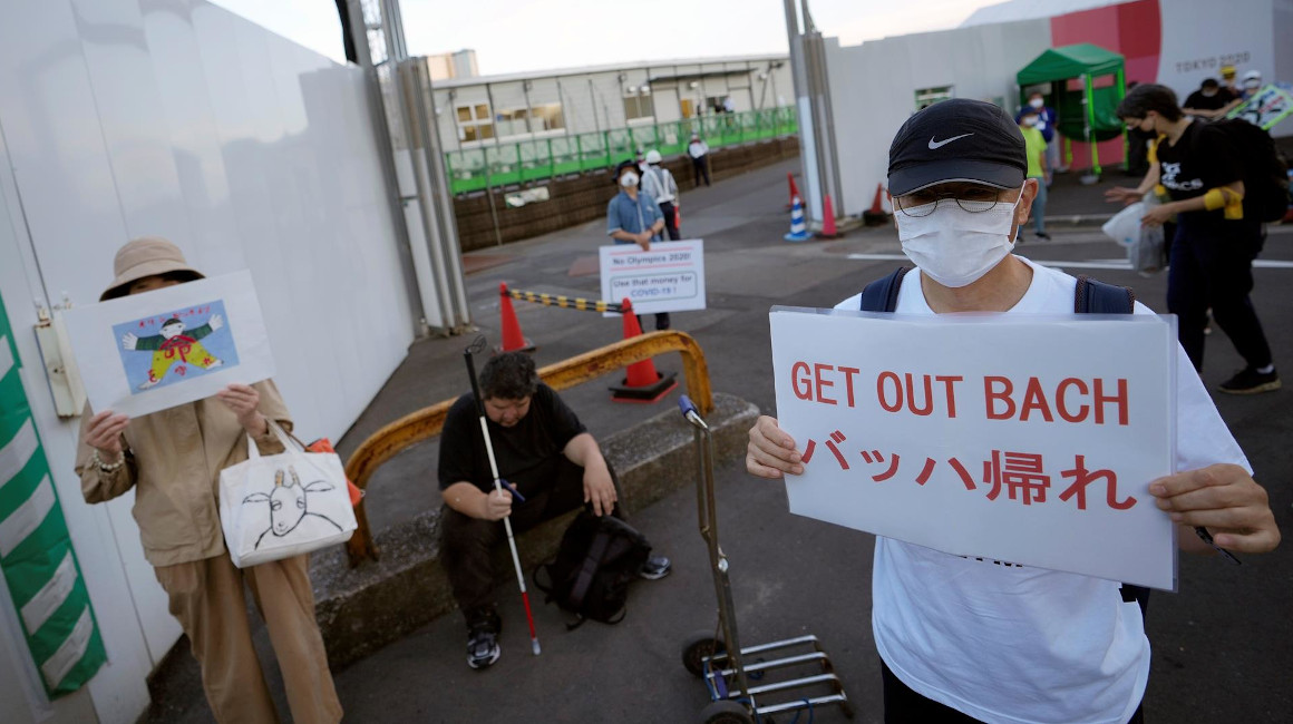 Personas muestran carteles en contra de Thomas Bach, presidente del COI, en Tokio, el 16 de julio de 2021.