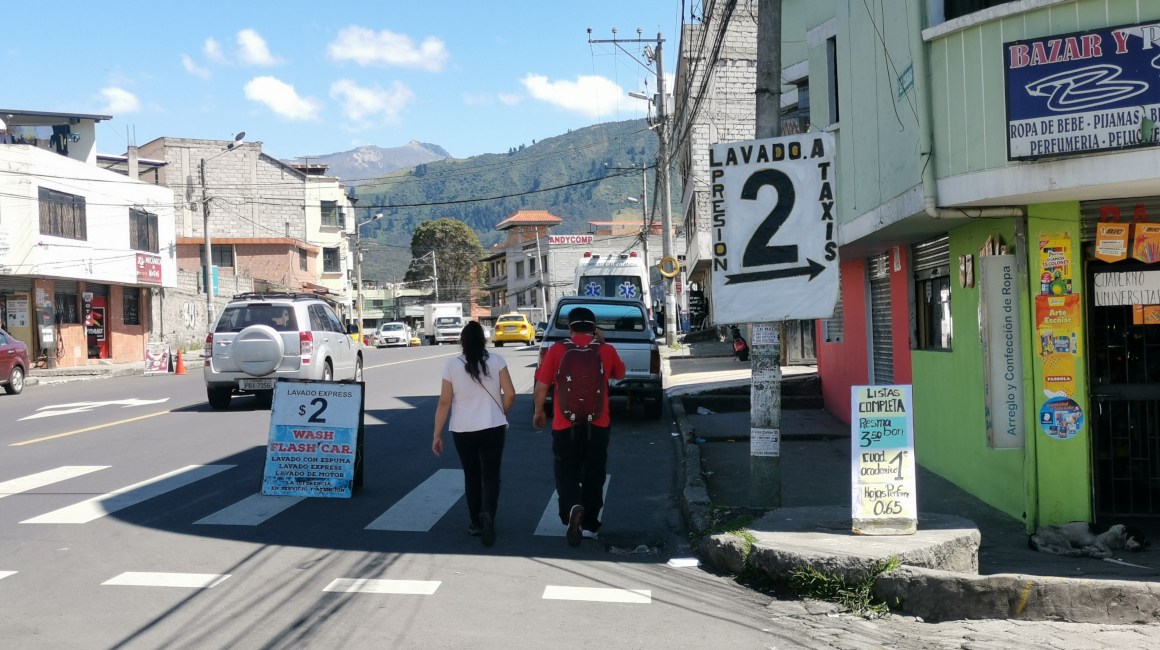 Dos personas caminan en medio de letreros que ofrecen lavado de autos, el 3 de septiembre de 2021.
