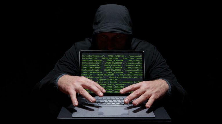 Un cibercriminal detrás de un computador que muestra información en códigos. 