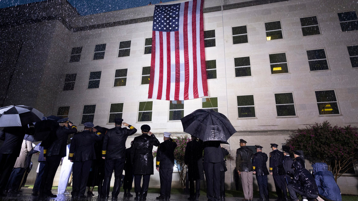 Supervivientes y miembros del Ejército escuchan el himno nacional junto a una bandera desplegada en el Pentágono, en Arlington, Virginia, Estados Unidos este domingo durante el 21 aniversario del atentado del 11-S.