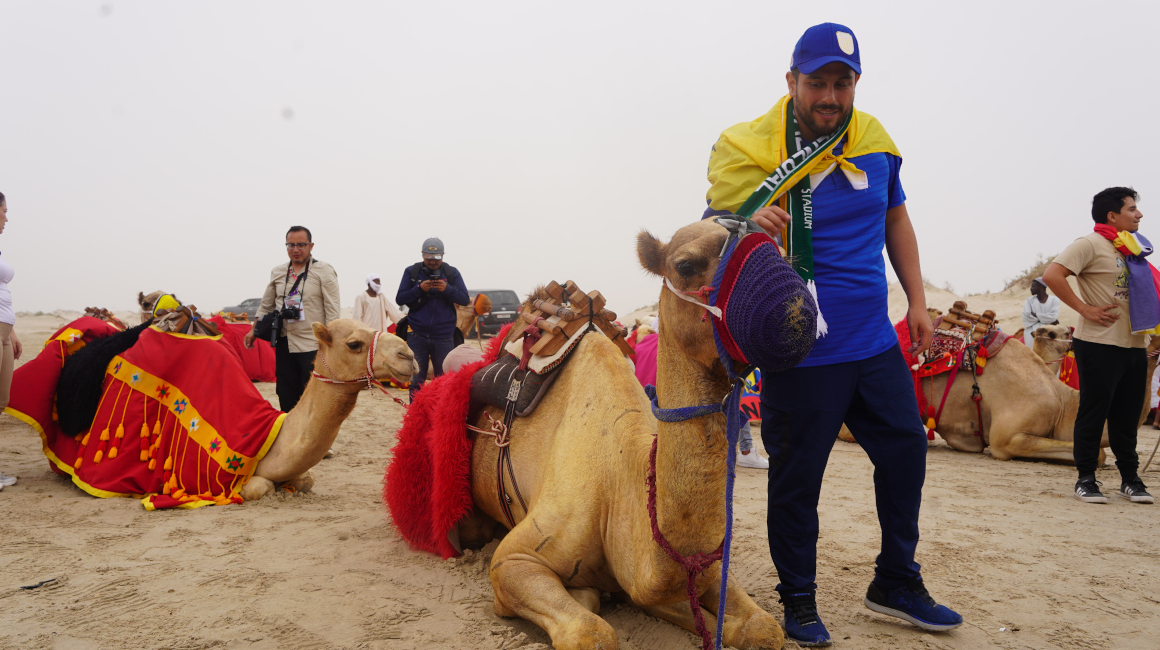 Un fanático con la bandera de Ecuador se acerca a un camello para tomarse una foto.