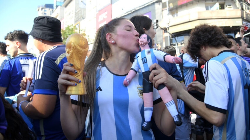 Seguidora con la camiseta de Argentina besa un muñeco de Messi y tiene una Copa del Mundo miniatura en su otra mano.