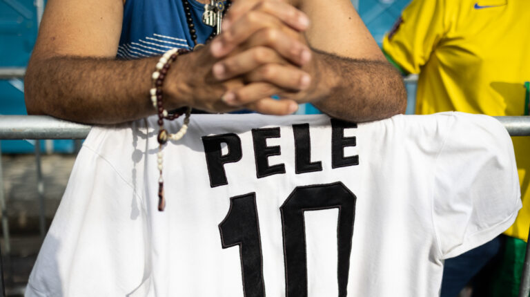 Seguidor de Pelé con un rosario un sus manos y la camiseta del astro brasileño mientras hace la fila para despedirlo.