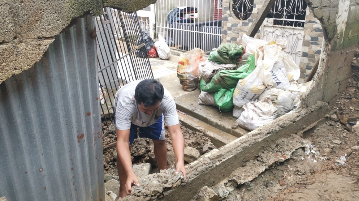 Un vecino de la urbanización Mercedes Molina, al norte de Guayaquil, coloca piedras y sacos en un muro colapsado ante el temor de nuevas lluvias.