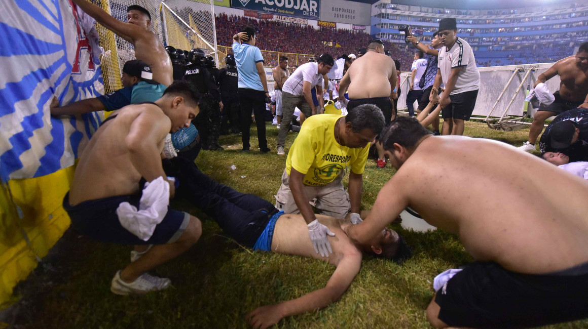 Aficionados auxilian a una persona tirada en el piso durante una estampida en El Salvador, el 20 de mayo de 2023.
