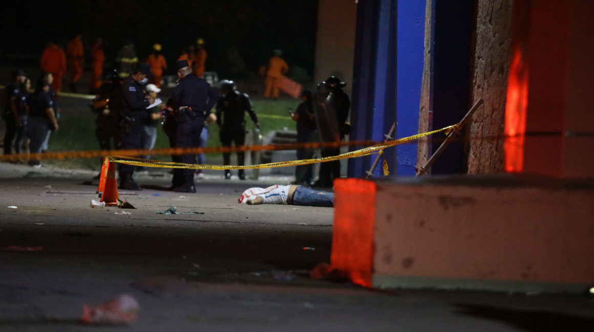 Miembros de la policía y primeros auxilios observan el cuerpo de una de las 12 personas que fallecieron en una estampida en El Salvador.