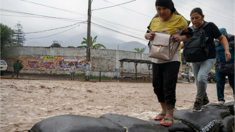Varias personas cruzan una vía en Chaclayo, Perú, durante unas inundaciones en marzo de 2023. 