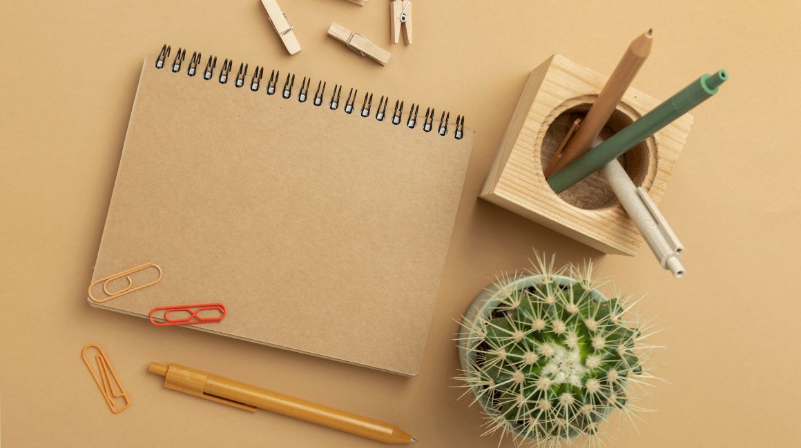 cuaderno ecológico a lado de un cactus con lapices y clip