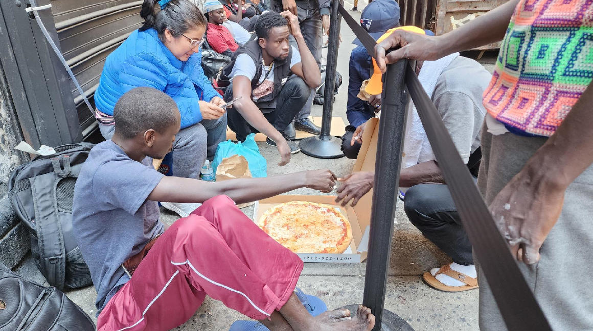 Migrantes comen pizza donada mientras hacen fila en espera de ser enviados a un albergue, el 31 de julio de 2023,, en Nueva York.