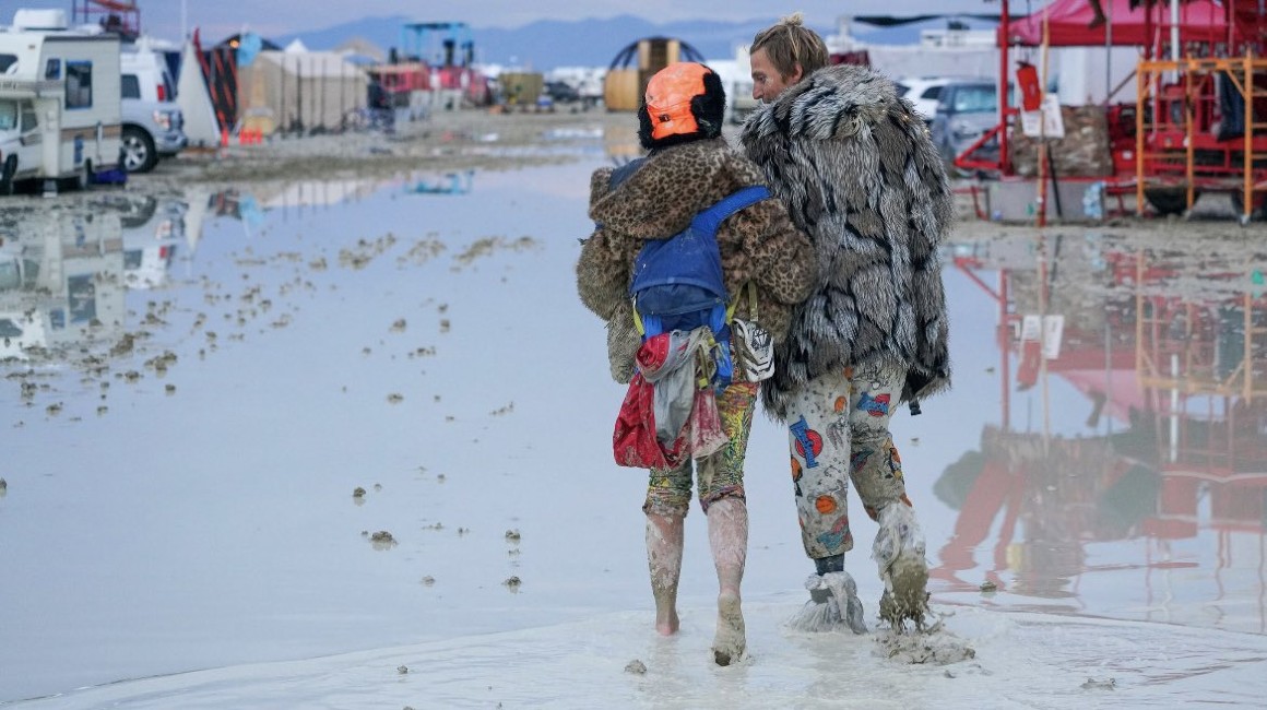 Dos personas caminan por el lodo del desierto de Nevada, luego de la lluvia que cayó sobre el festival Burning Man.