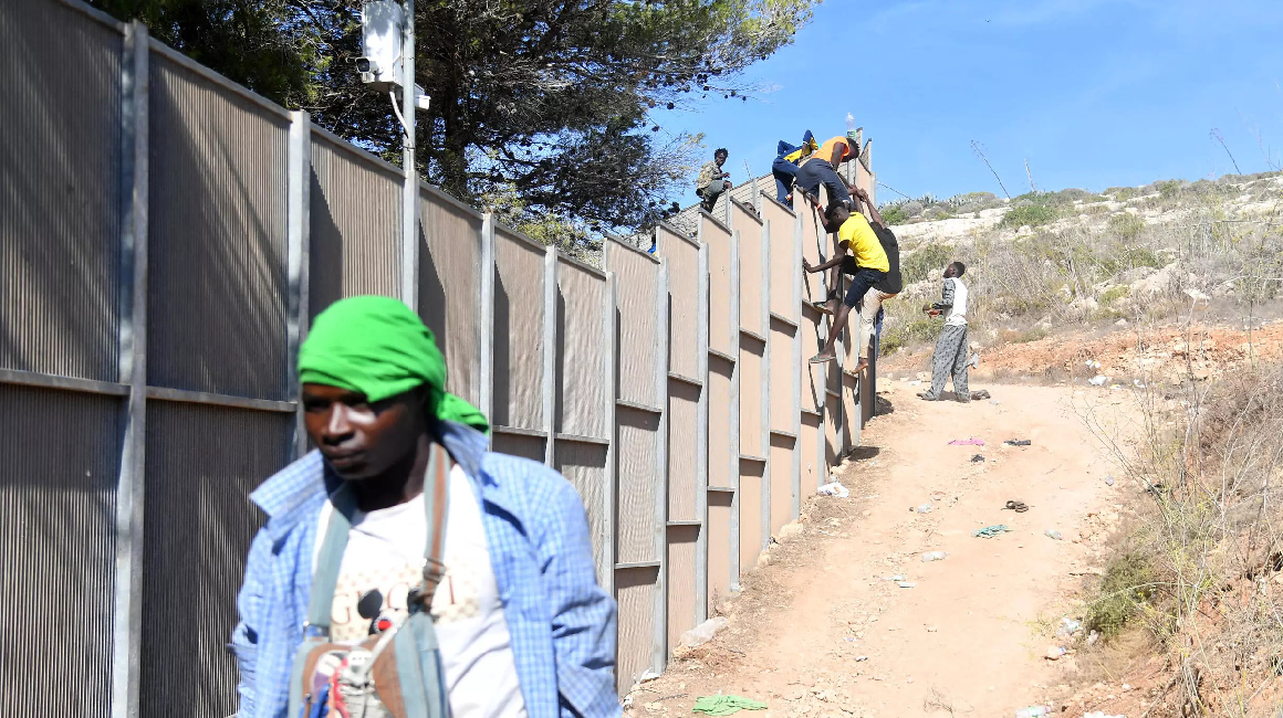 Migrantes cruzan la valla para salir del centro de acogida de la isla italiana de Lampedusa, el 14 de septiembre de 2023.