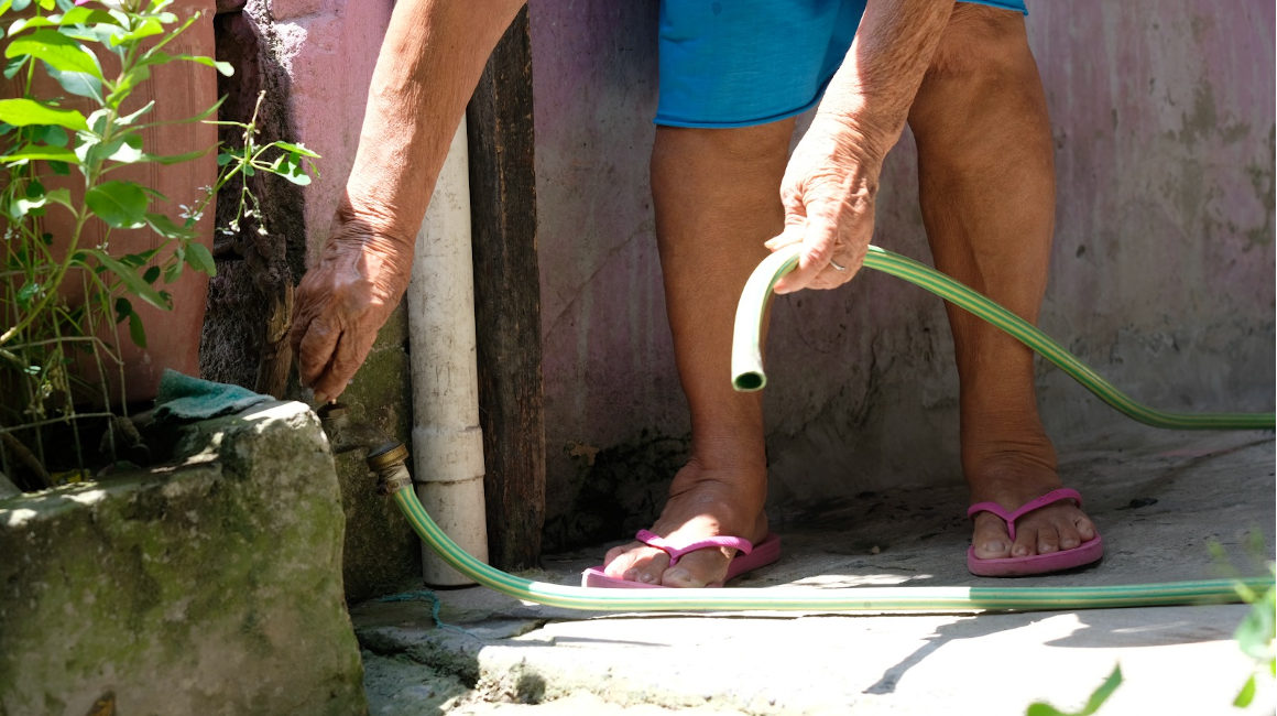 Una mujer abre la llave de  una manguera durante un corte de agua en el cantón Sucre, en Manabí.