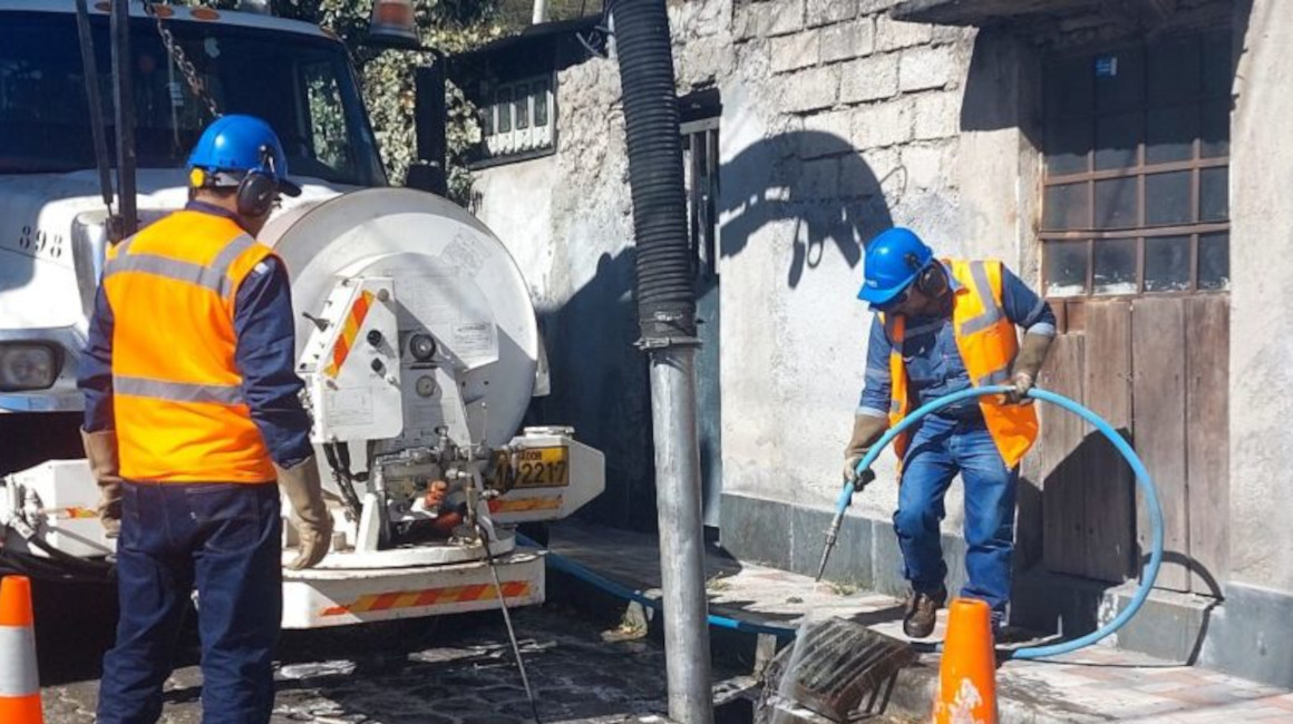 Dos trabajadores de la Epmaps limpian una alcantrilla en Quito, en octubre de 2023.