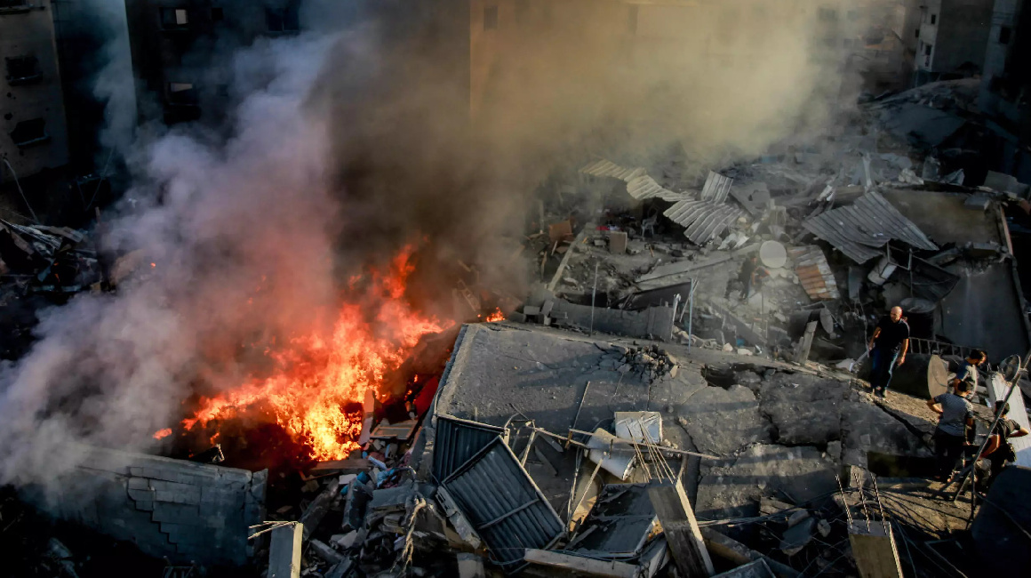 Algunos palestinos buscan entre los escombros de un edificio arrasado mientras el humo y el fuego se elevan tras un ataque israelí, en la ciudad de Gaza el 26 de octubre de 2023, en medio de la guerra entre Israel y el grupo Hamás.