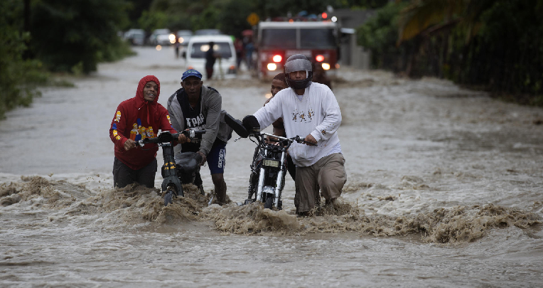 Personas cruzan con dificultad la carretera que se encuentra inundada producto de las intensas lluvias.