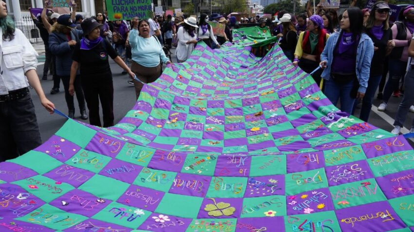 Un grupo de mujeres lleva un telar bordado con los nombres de las víctimas de femicidio.