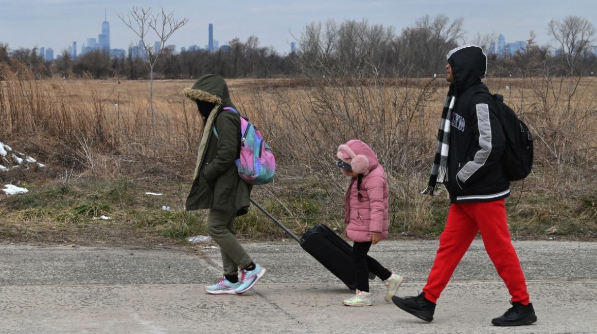 Migrantes recién llegados caminan hasta una parada de autobús frente al refugio Floyd Bennett Field el 21 de febrero de 2024 en el distrito de Brooklyn de Nueva York.