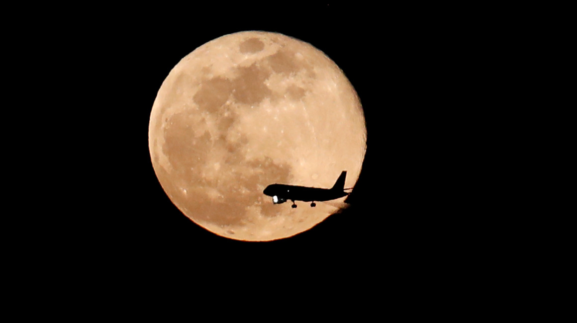 Un avión pasa ante la luna llena de abril, también conocida como "luna rosada", en 2017.