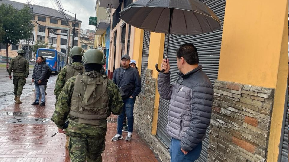 Un hombre se resguarda de la lluvia, mientras militares patrullan en el centro de Quito, el 29 de marzo de 2024.