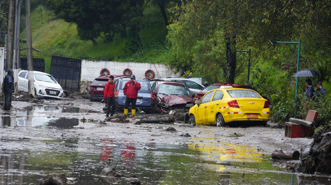 Dos personas en medio del agua y escombros que dejó el aluvión en La Gasca, en el norte de Quito, el 2 de abril de 2024.
