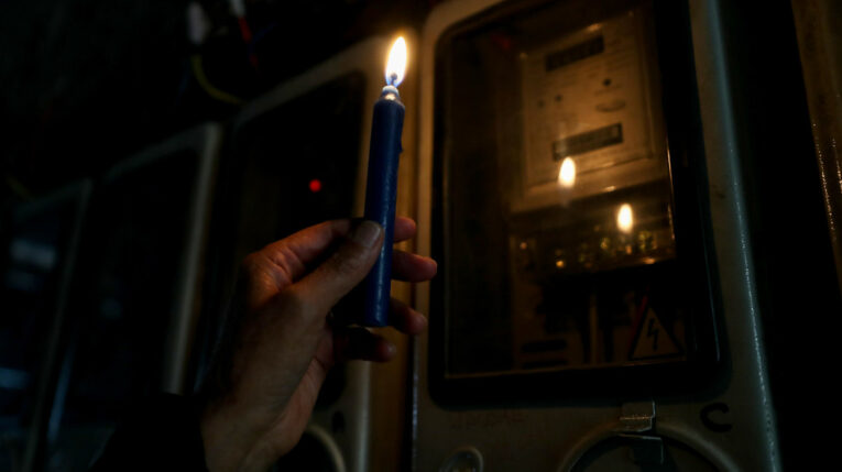 Imagen referencial de un ciudadano con una vela prendida revisando un medidor de luz. 
