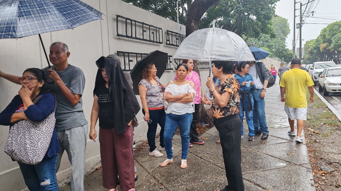 Varias personas esperan bajo la lluvia en los exteriores de un colegio en Guayaquil, el 21 de abril de 2024.