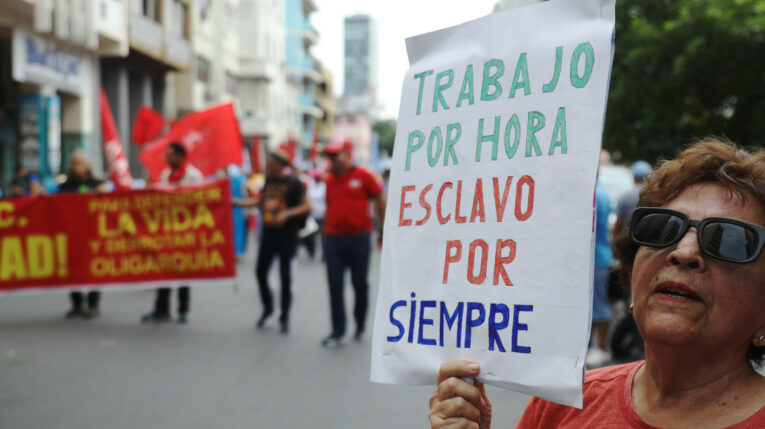 Una mujer porta un letrero en contra del trabajo por horas, durante la marcha del Día del Trabajador, en Guayaquil, el 1 de mayo de 2024.