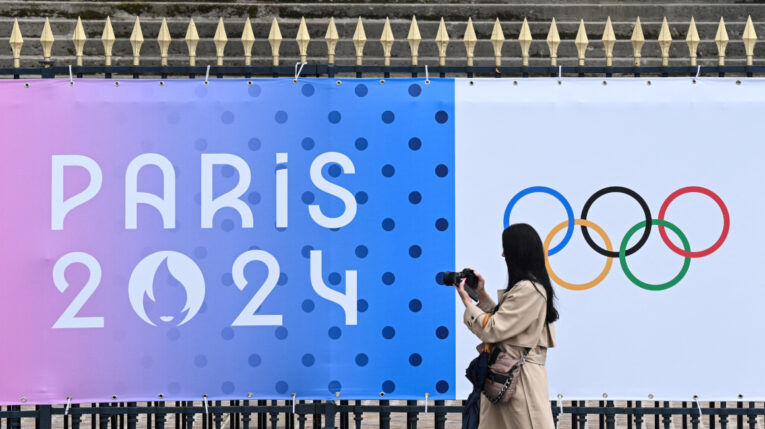 Transeúnte toma una fotografía de una pancarta de los próximos Juegos Olímpicos de París 2024 frente a la Asamblea Nacional en París, el 5 de mayo de 2024.