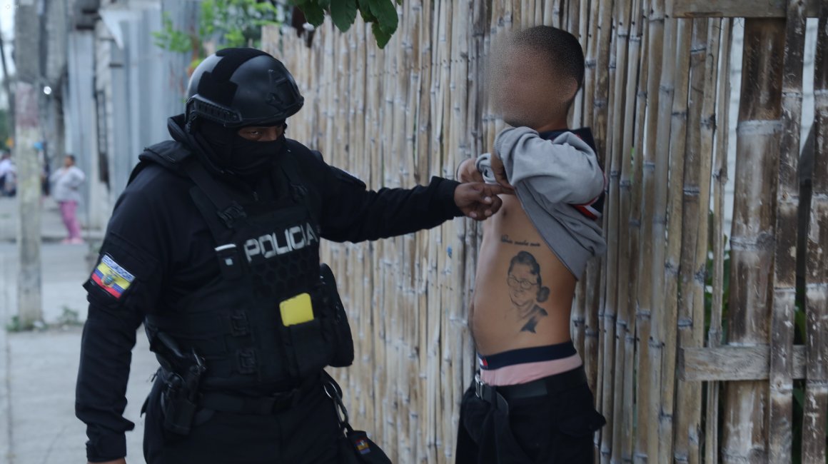 Un policía revisa los tatuajes de un sospechoso durante un operativo que incluyó 19 allanamientos en Durán, el martes 11 de junio del 2024.